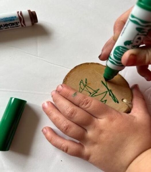 child drawing with a green marker on a wood cookie